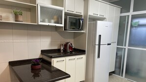 Uma cozinha com armários brancos, bancada preta, micro-ondas, geladeira e uma pequena mesa com um vaso de planta.