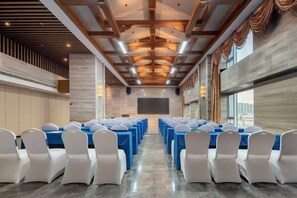 A conference room with rows of tables and chairs, a large screen, and a modern ceiling design.