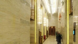 Un pasillo con paredes de mármol, una puerta de madera al final y una planta en maceta.