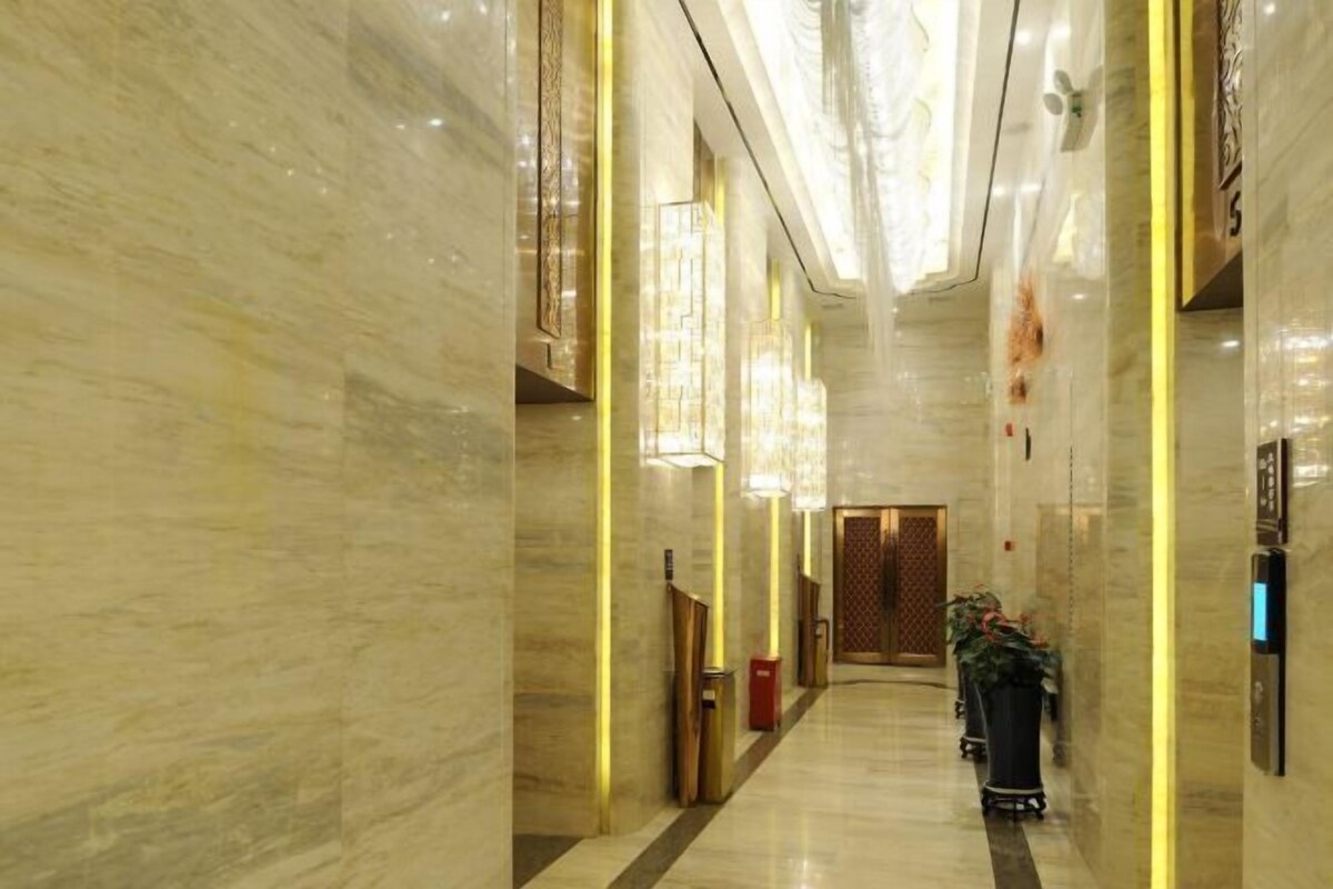 A corridor with marble walls, a wooden door at the end, and a potted plant.