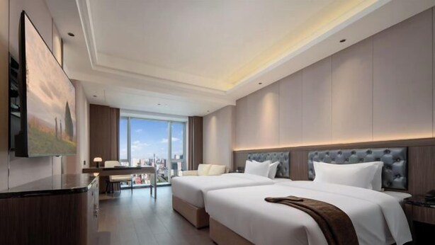 Habitación de hotel con dos camas, un escritorio y un amplio ventanal con vistas a la ciudad.
