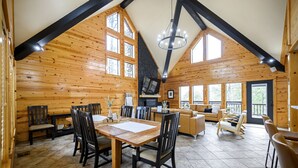 Een ruime houten hut met een eethoek, woonkamer en grote ramen.