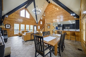 Una cabaña de madera espaciosa con comedor, cocina y una escalera que sube a un nivel superior.