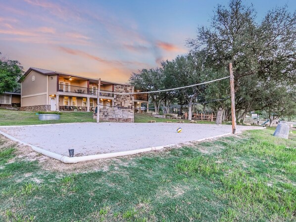 Hotel con zona de patio que incluye una cancha de voleibol, rodeado de árboles y un edificio con varios balcones.