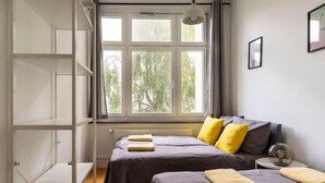 Une chambre avec deux lits, une fenêtre donnant sur les arbres et une étagère blanche.