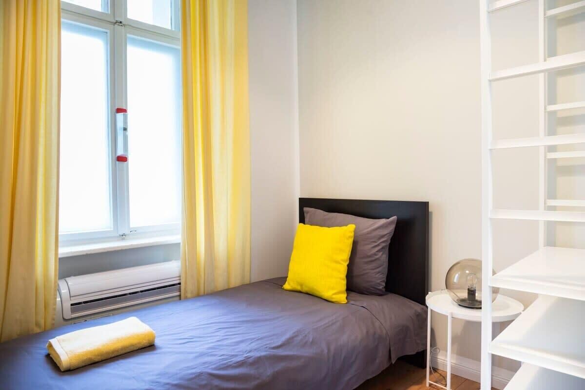 Una camera da letto ordinata con un letto, un comodino con una lampada e una finestra con tende.