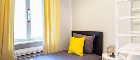 Una camera da letto ordinata con un letto, un comodino con una lampada e una finestra con tende.