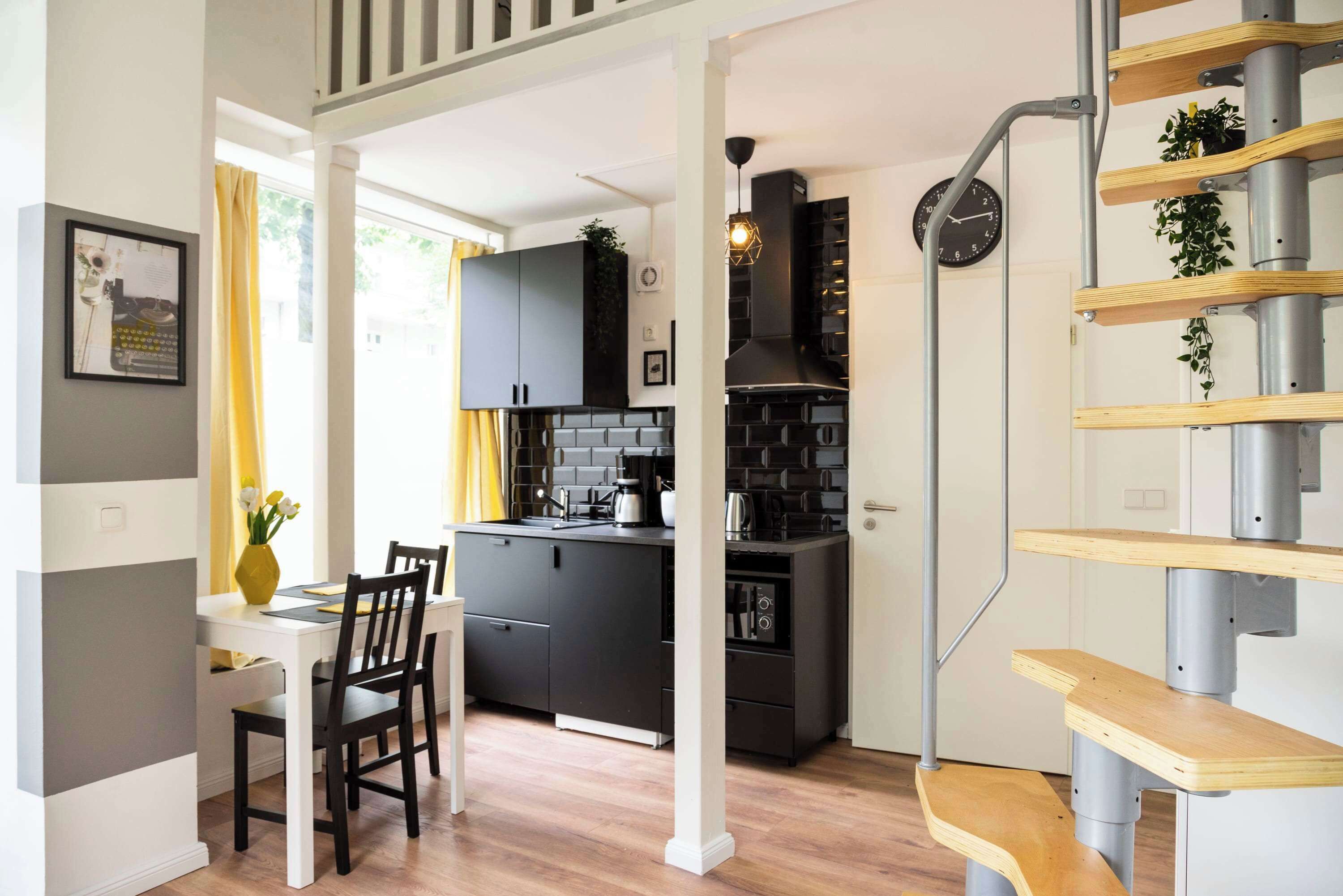 A modern kitchen with black cabinets, a wooden dining table, and a staircase with wooden steps.