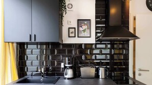 A modern kitchen with black cabinets, a black tiled backsplash, a coffee maker, a toaster, and a kettle on the counter. - Charmante Wohnung in Berlin-Wilmersdorf (Berlin)