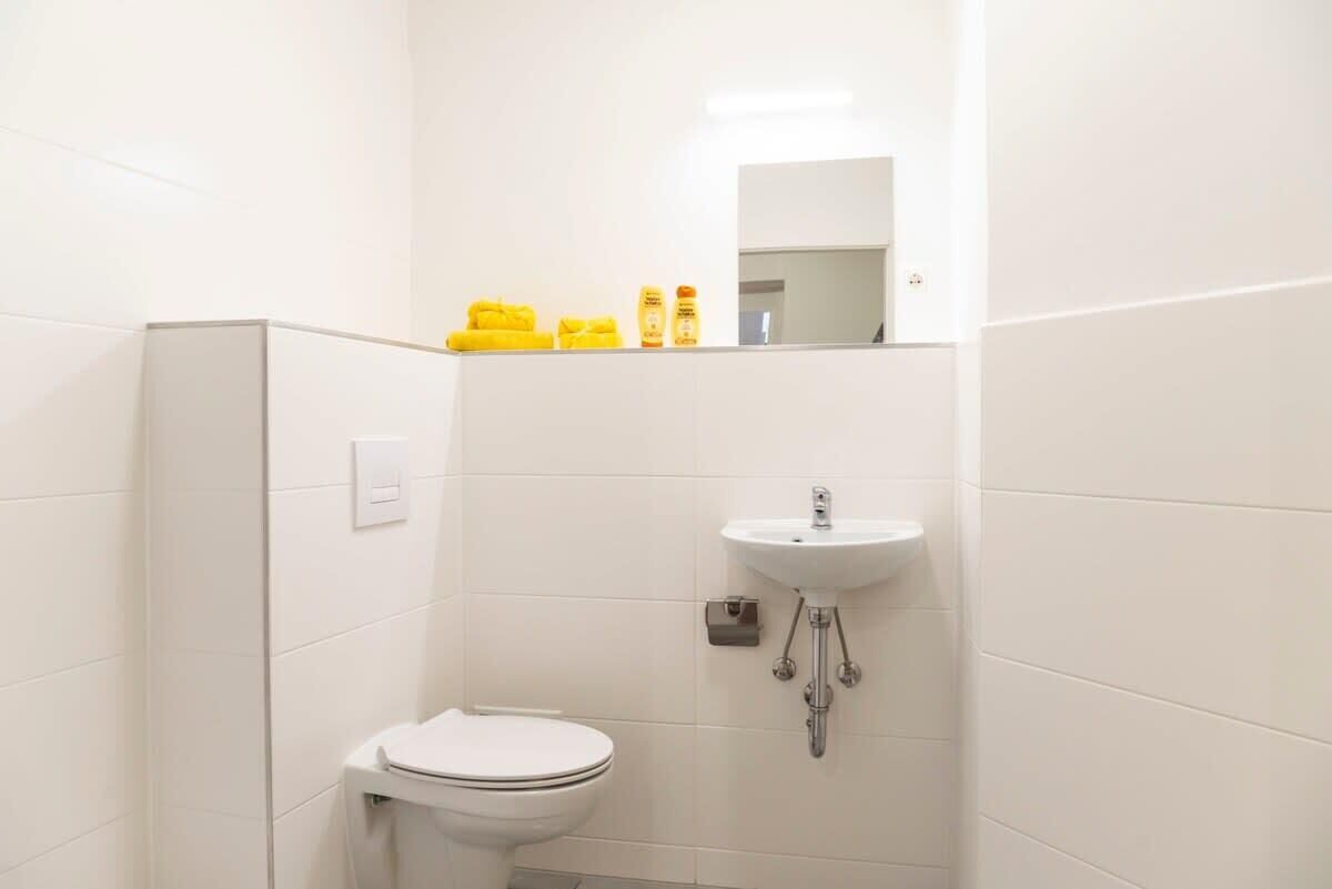 Ein kleines, weißes Badezimmer mit Toilette, Waschbecken und Spiegel.