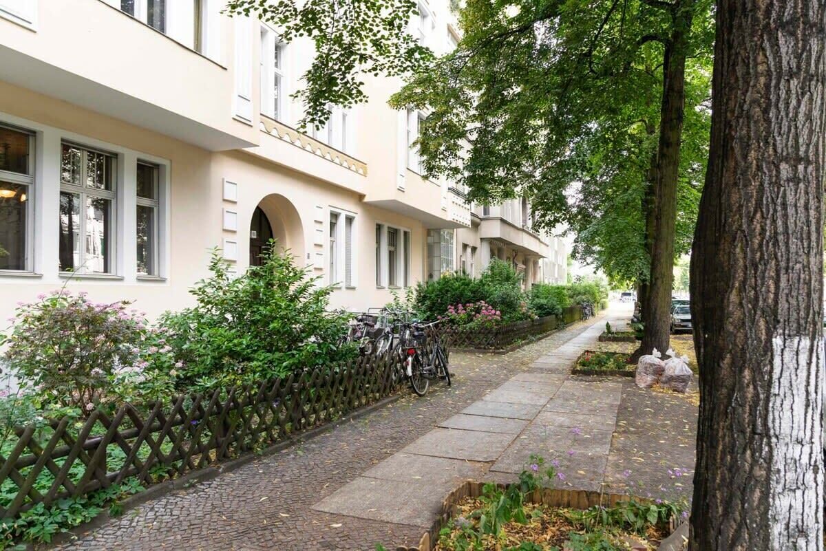Een rij herenhuisjes met een geplaveid pad, een fiets en een trottoir met bomen.