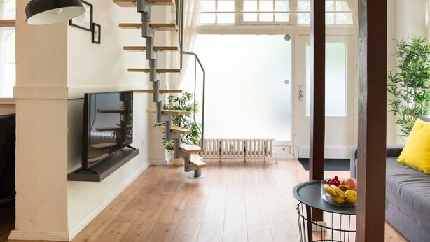A modern living room with a wooden staircase, a fireplace, and a dining area with a fruit bowl. - Stylish Loft Apartment (Berlin)