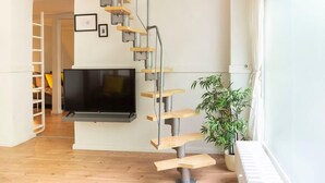 A modern living room with a wooden staircase, a flat-screen TV, and a potted plant. - Stylish Loft Apartment (Berlin)