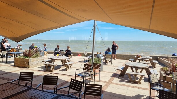 An outdoor patio with tables and chairs, overlooking a body of water.