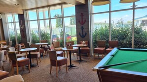 A pool table in a room with large windows, chairs, and tables.