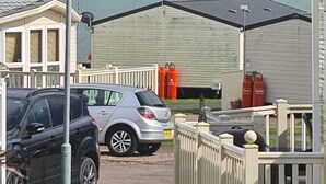 A caravan park with caravans, a car, and a view of the sea.