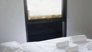 Een hotelkamer met een bed, witte lakens en een raam met uitzicht op gebouwen.