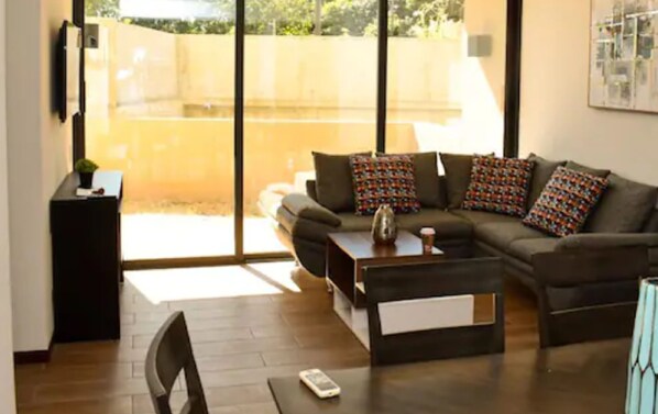 A modern living room with a sectional sofa, a coffee table, and a small side table. - Infinity Pool Apartment (San Salvador)
