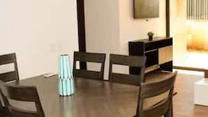 Un comedor con una mesa y sillas de madera, un pequeño jarrón decorativo y un televisor montado en la pared.