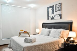 A hotel room with a bed, bedside lamps, a tray with fruit and juice, and a painting on the wall. - Infinity Pool Apartment (San Salvador)
