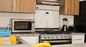 Een keuken met een fornuis, oven, magnetron en blender op het aanrecht.