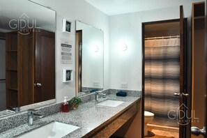 A bathroom with a granite countertop, two sinks, a large mirror, and a striped shower curtain. - Infinity Pool Apartment (San Salvador)