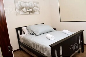 Een slaapkamer met een bed, kussens en een kunstwerk aan de muur.