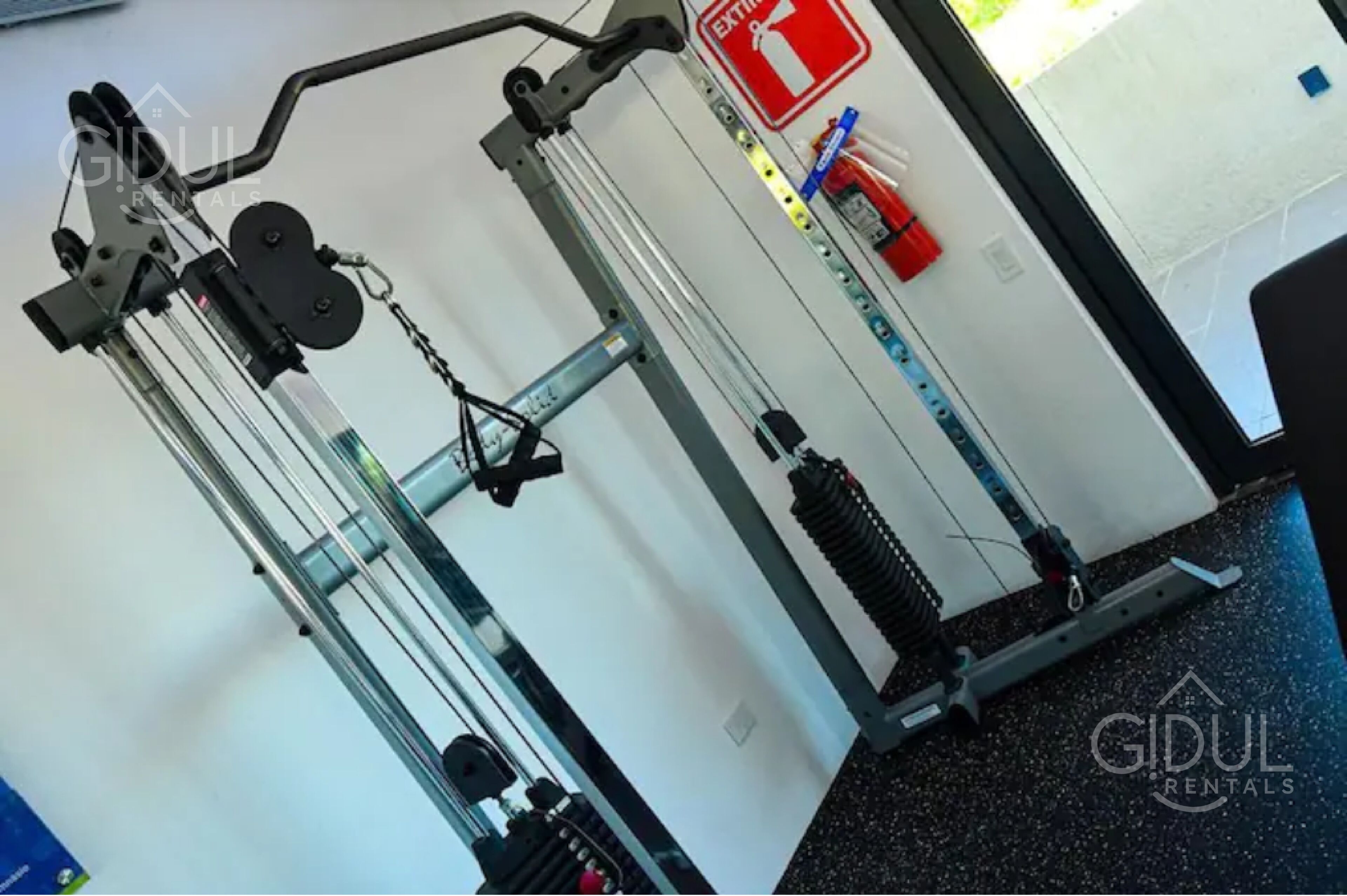 A gym with exercise equipment, a fire exit sign, and a water bottle on the wall.