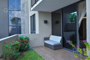 Un área de estar moderna al aire libre, con un banco acolchado, una mesita y una planta en maceta.
