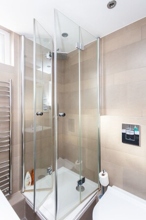 A modern bathroom with a glass-enclosed shower, a towel rack, and a wall-mounted sink with a soap dispenser. - Spacious Central 3 Bedroom Apartment in Old Street (London)