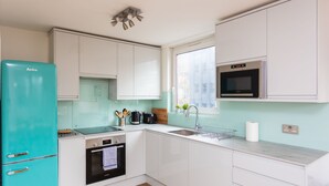 Una cocina moderna con armarios blancos, un refrigerador turquesa, horno empotrado y microondas.