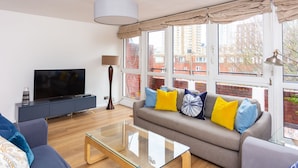 Una sala de estar moderna con sofá, televisión y una mesa de centro de vidrio.