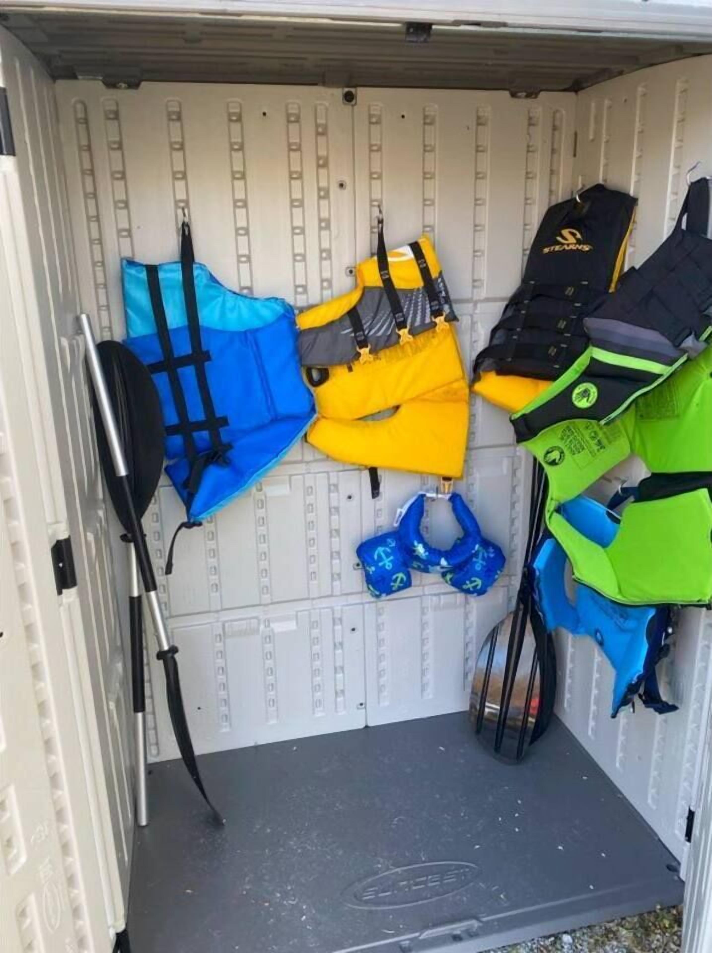 Un espace de rangement contenant différents gilets de sauvetage et une planche de paddle.