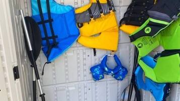 Un espace de rangement contenant différents gilets de sauvetage et une planche de paddle.