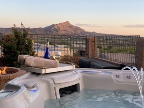 A hot tub with a view of mountains, a bottle, and a glass of white wine.