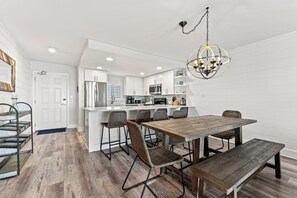 A modern kitchen with white cabinetry, a wooden dining table with chairs, and a hanging light fixture.