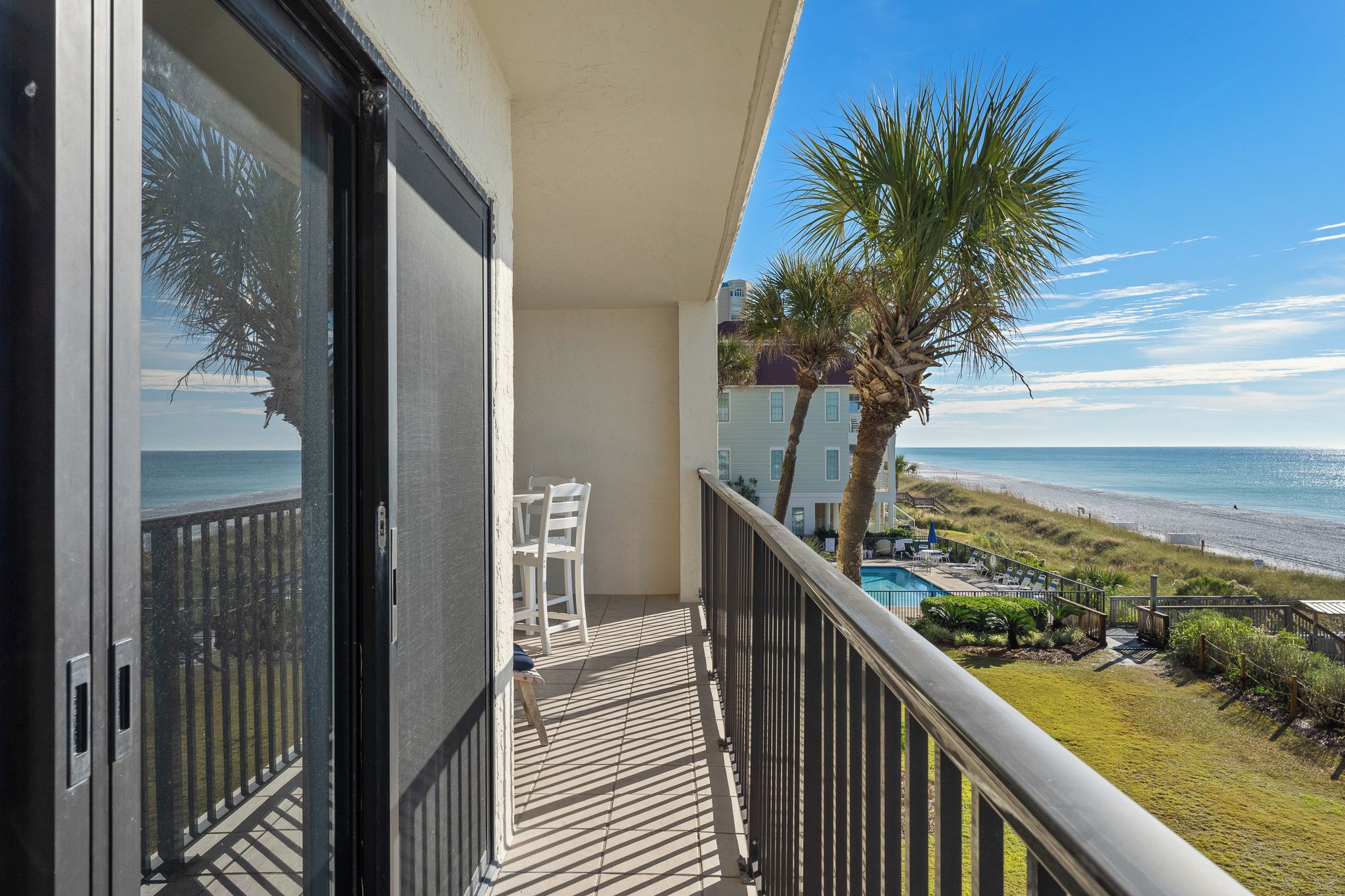 Un balcon avec vue sur la plage, une piscine et un palmier.