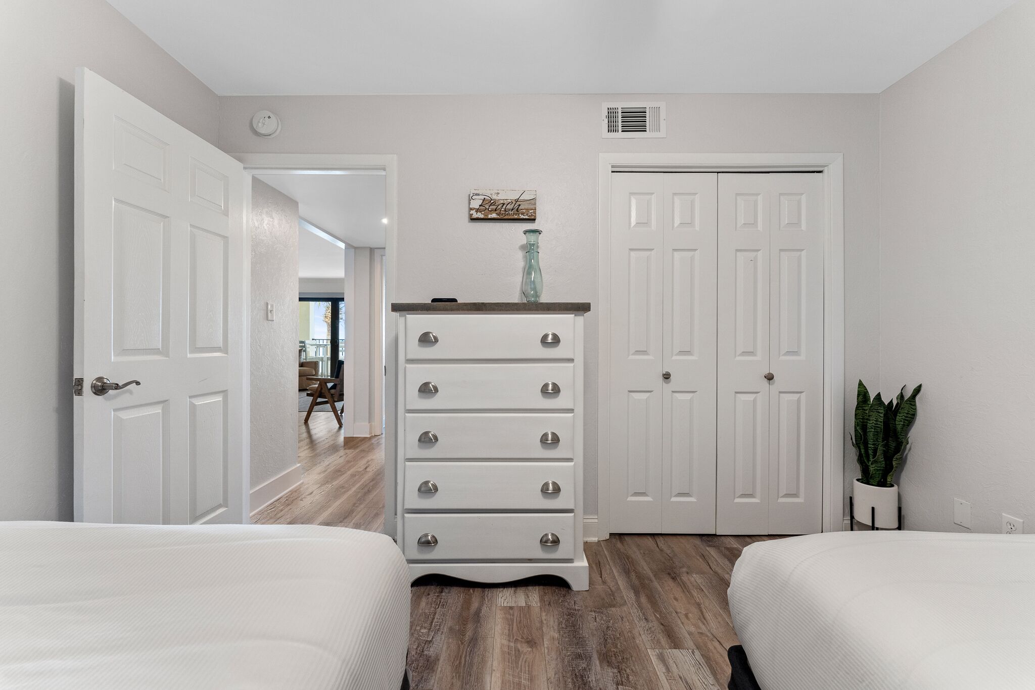 A bedroom with two beds, a dresser, a closet, and a plant.