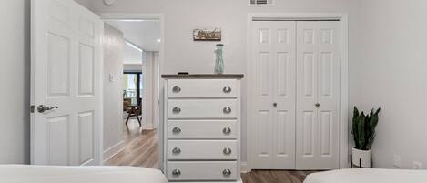 A bedroom with two beds, a dresser, a closet, and a plant.