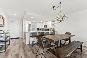 A modern kitchen with white cabinetry, a wooden dining table with chairs, and a hanging light fixture. - Huntington By the Sea 306. Gulf Front, Community Pool, Free Beach Service. (Miramar Beach)