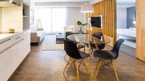 A modern kitchen with white cabinets, a dining area with a glass table and black chairs, and a wooden partition with a TV. - Soho Apartments in Miraflores by Wynwood-House (Lima)