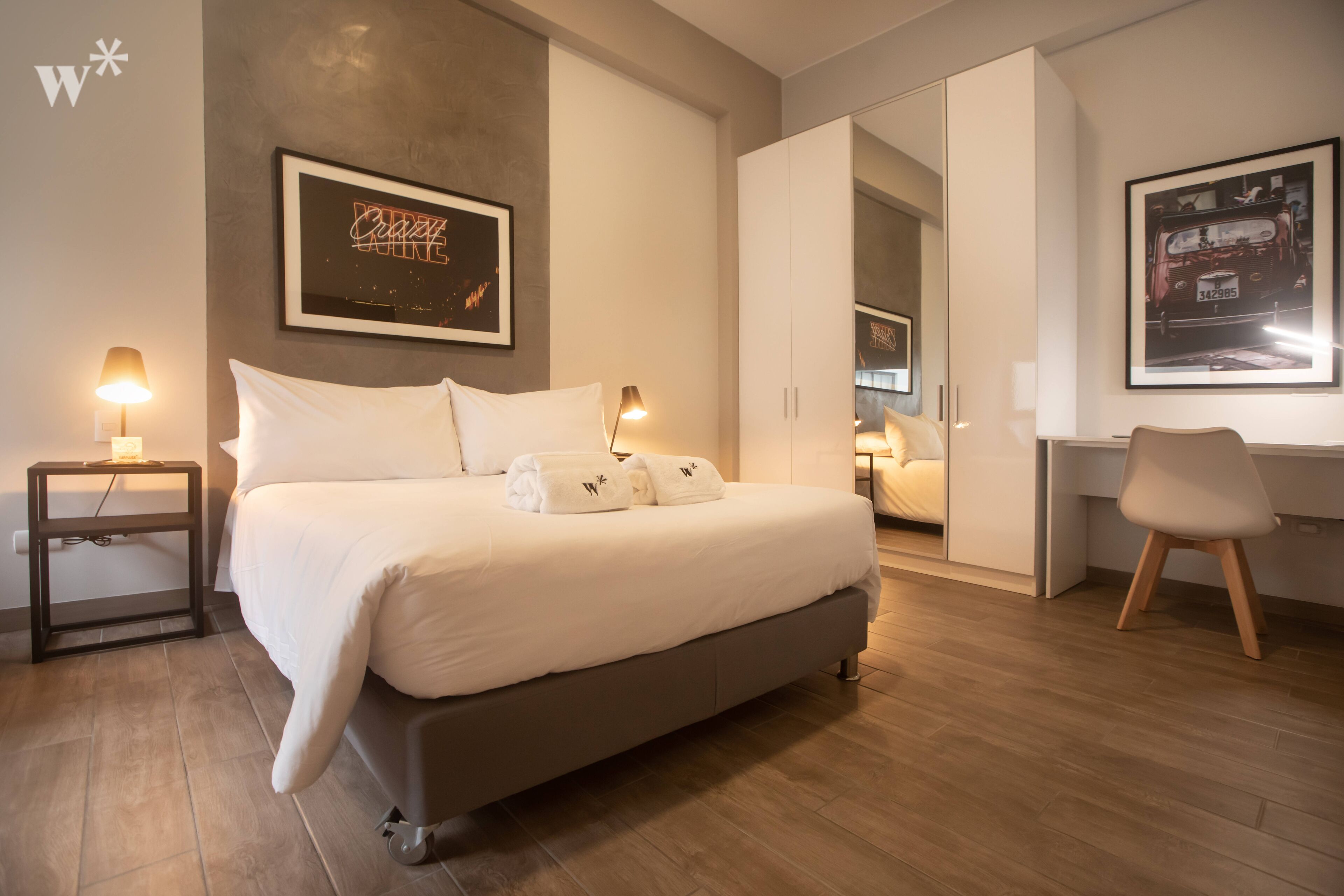 Een moderne slaapkamer met een groot bed, nachtlampjes, een bureau en een stoel.