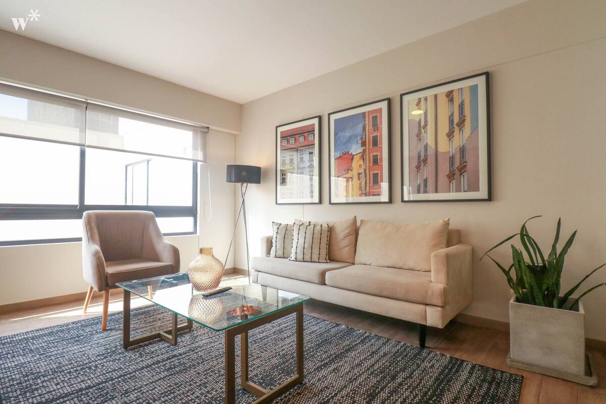 Ein modernes Wohnzimmer mit einem Glastisch, einem beige gefärbten Sofa und einem großen Fenster.