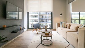 A modern living room with a sofa, a coffee table, a TV mounted on the wall, and a large window with a view of buildings. - Soho Apartments in Miraflores by Wynwood-House (Lima)