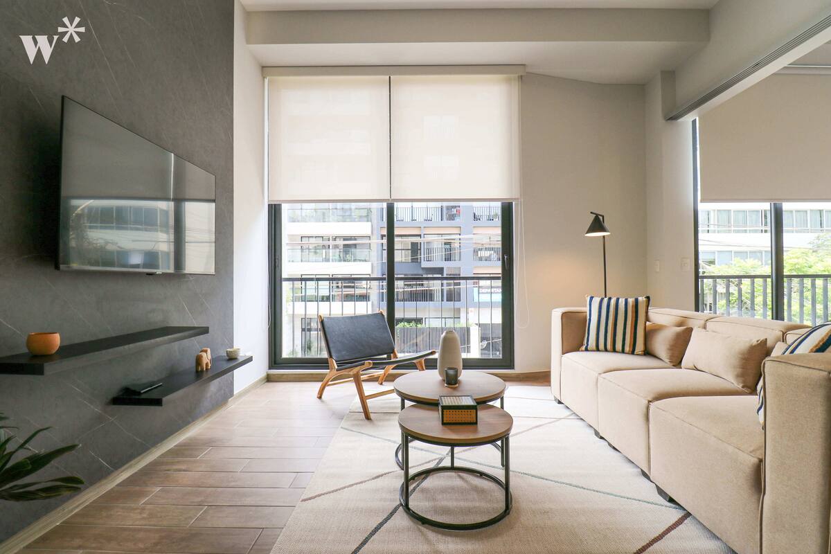 Ein modernes Wohnzimmer mit einer Couch, einem Couchtisch, einem an der Wand montierten Fernseher und einem großen Fenster mit Blick auf Gebäude.