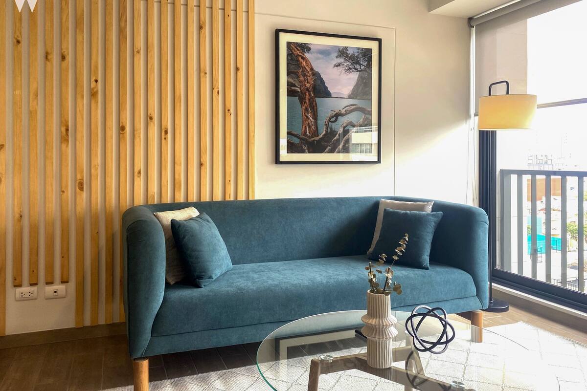 Ein modernes Wohnzimmer mit einem blauen Sofa, einem Glastisch und einer Wand aus Holzlatten.