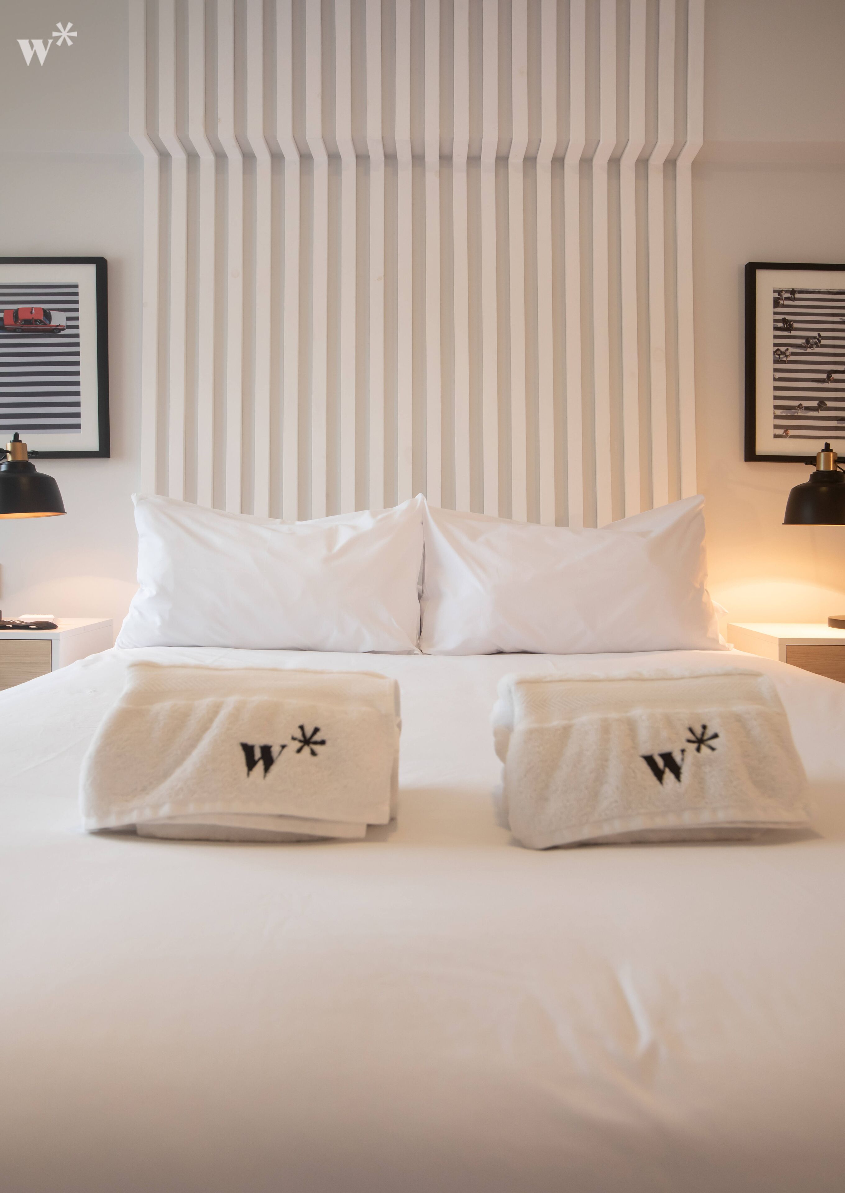 A neatly made bed with white linens and two towels with a logo on them.