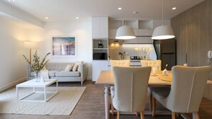 A modern living room with a sofa, coffee table, and dining area with chairs. There is a kitchen in the background with cabinets and appliances. - Soho Apartments in Miraflores by Wynwood-House (Lima)