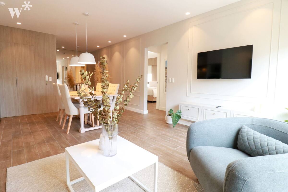 Ein modernes Wohnzimmer mit einem grauen Sofa, einem weißen Couchtisch und einem Essbereich mit weißem Tisch und Stühlen.