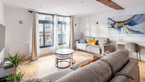 Ein modernes Wohnzimmer mit einem grauen Sofa, einem runden Couchtisch und einem großen Fenster mit Vorhängen.